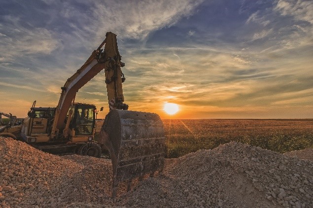 Backhoe digging into dirt at sunset